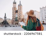 Attractive young female tourist is exploring new city. Redhead girl holding a paper map on Market Square in Krakow. Traveling Europe in autumn. St. Marys Basilica