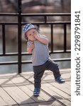 Small photo of European toddler child in a panama hat sucks his thumb and makes unsteady steps on the terrace in spring