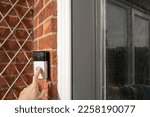 Small photo of London, UK - Circa February 2023: Neighbour seen pressing a popular, wireless smart door bell at the front of the house, outside the porch. The door bell is connected to an internal ringer device.