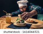 Small photo of chef finishing up his vegan burger with lettuce tomato and sauce, fries with ketchup and healthy drink on a wooden table, vegetarian food and foodie lifestyle concept, selective focus