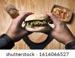 Small photo of man's hands holding a vegan burger to eat it, healthy food and foodie lifestyle concept, pov image, subjective point of view, selective focus