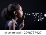  A studio portrait of a 10-year-old African American girl of Ethiopian descent blowing bubbles, with her curly hair in a ponytail and a black background adding contrast.
