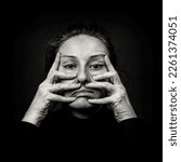 Small photo of Conceptual dark portrait of old woman stretching the skin of her face in ugly grimace. Problems with skin and wrinkles, demonstration against plastic surgery. Black and White film grain.