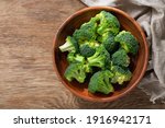 Bowl of fresh broccoli florets on wooden background, top view