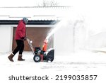 Snow blower powered by gasoline in action. Man outdoor in front of house using snowblower machine. Snow removal, thrower assistant in winter outside home. Young worker guy blowing snow during blizzard
