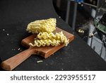 Small photo of Block of uncooked noodles with a wooden butting block on a black background in studio ZUVJSUX