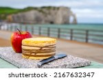 Small photo of Tasting of yellow livarot cow cheese from Calvados department served with apple and view on alebaster cliffs Porte d'Aval in Etretat, Normandy, France