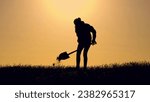 Small photo of Woman digging pit with shovel dark silhouette in farm field at sunset. Woman digs ground in field against sky lit by sunset. Woman works digging soil with shovel in country field in spring evening