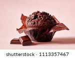 Chocolate muffin in brown paper with chocolate pieces on pink background