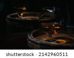 Small photo of Brandy-alcoholic drink stands on wooden barrel full of brandy illuminated by soft dim light in style of rustic. Old barrel of cognac stands in wine cellar. Wine alcoholic strong drink brandy.