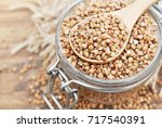Wooden spoon of roasted buckwheat on buckwheat groat jar background, gluten free ancient grain for healthy diet, selective focus