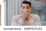 Small photo of Hispanic man scared businessman boss stands in city covering mouth with hands from shock fear blab out secret frightened face expression. Brunette guy makes gesture of shock amazed sign outdoors
