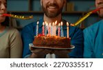 Small photo of Cropped view caucasian adult happy bearded man celebrate birthday at home diverse african caucasian friends congratulate male with festive cake blowing party whistles make surprise annual tradition