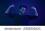 Small photo of Funny Indian man slim guy fooling around show hands muscle biceps sport strong power bodybuilder ultraviolet neon studio background proud champion boast efficient security coding achievement level up