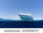 Small photo of luxury boat sitting on anchor floating in deep blue water with blue sunny skies in background. Split shot of the bow and anchor line of luxury boat as it floats in the ocean in the Bahamas.