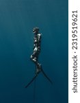 Small photo of Speardiver swimming to surface with spear in one hand wearing camouflage wetsuit, water is deep blue and clear with sun rays shining through around freediver swimming to surface in Bahamas.