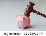 Small photo of Judge wooden gavel is brought over piggy bank isolated over white background. Bank account arrest concept