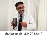 Indian Male doctor in a white coat in a modern clinic reads using  Smart phone with happy and smiles. Asian healthcare concepts