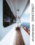 Small photo of A wide-angle vertical shot of the side-deck of a luxurious white safari boat with a row of windows of the deckhouse wooden floor of the ways and the waterscape astern with a blue sea water