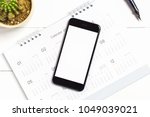 Top view of smart phone isolated white screen for mockup design or app display with calendar and pen on white wooden background