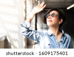 Small photo of Beautiful / Stylish Asian woman wearing 100% UV light eyes protection sunglasses, stand and raise her hand to block out bright glare and sunlight from outside to avoid ultraviolet rays over exposure.
