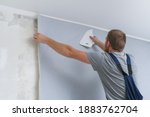 Wallpapering. A man glues gray vinyl wallpaper on a non-woven backing. Renovation of the room. Hang wallpaper. Home repairs.