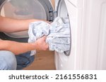 Small photo of tumble dryer. A man takes dried bed linen out of the tumble dryer. Dryer machine in the house.