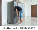 Small photo of On a hot day, the guy cool down with his head in the refrigerator. Broken air conditioner.