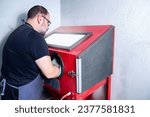 Small photo of general shot of a luthier at a sandblasting machine for polishing small musical instrument keys in a brass musical instrument repair shop
