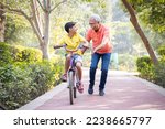 Small photo of Grandfather trying to teach grandson to ride a cycle at park.