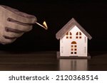 Small photo of Model house and hand in glove with matchstick on a black background. Concept risk of accident with fire. Arsonist Criminal.
