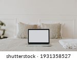 Laptop with blank copy space screen display in bed with plaid, pillows against white wall. Aesthetic morning composition. Freelancer, outsourcing minimalist home business, work concept.
