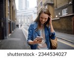 Young woman using a smart phone while walking down a sidewalk in London