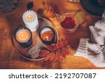 Flat lay with cozy warm sweater, herbal tea in glass cup, burning candles and autumn fall leaves on yellow blanket. Autumn mood, hygge concept