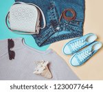 Women's clothing, shoes and accessories on a blue yellow pastel background. Fashionable look. Sneakers, sweater, jeans, bag, sunglasses, belt, shell. Top view. The trend of minimalism.