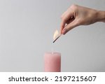 Woman's hand with match sets fire to scented pink wax candle on a gray background