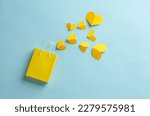 Miniature yellow shopping bag with hearts on blue background. Sale, love, shopping concept. Creative layout