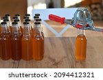 Small photo of Hand capper on the background of brown bottles with homemade liquor or alcohol. Home brewing.