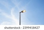 Small photo of Location photos Tall black light pole on the side of the road Alone in the middle of the picture Has a warm yellow light. The background is faint clouds under the evening blue sky. The atmosphere