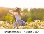 Girl running on the field of dandelions on sunset. Beautiful little kid dancing on dandelion meadow. Summer fun outdoors.