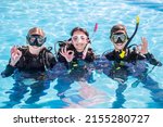 A group of happy scuba divers smiling at the camera with their dive masks and gear on in a pool showing the OK sign