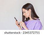 Small photo of young pretty Caucasian woman in a purple T-shirt is excited and holding in her hand.She received an unpleasant message,frowns, worries and anxiously writes reply message.isolated on a light background
