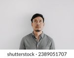Small photo of Close up of Asian man with beard wear grey t-shirt emotionless face, looking above space isolated over white background wall.