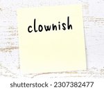 Small photo of Yellow sticky note on wooden wall with handwritten inscription clownish