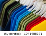 Colorful t-shirts on hang for sale in shop. Multicolored summer top on hanger. Summer season clothes department store. Unisex apparel for warm weather. Summer sale in shopping mall. Rainbow tshirts