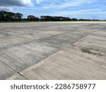 Empty airport field with green forest behind. Concrete field for transport and logistic services. Spacious asphalt field photo background. Airstrip summer landscape. Summer vacation travel in Asia