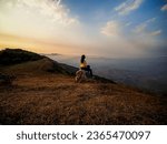 Small photo of Alone tourist on the edge of cliff and watching into deep valley bellow at Phu Bak Dai, Loei, Thailand. Woman sit alone at the cliff of mountain to see scenic view of sunset and range of mountain.