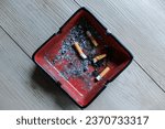 Small photo of Top view of cigarette stubs in red ashtray. Warning, smoking addiction and health risk.