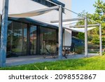 Small photo of Detail of terrace of modern, white, cube, elegant, minimalist style passive house with large panoramic windows, grey shutters in maintained garden.