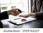 Small photo of A car rental company employee is handing out the car keys to the renter after discussing the rental details and conditions together with the renter signing a car rental agreement. Concept car rental.